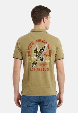 Homme portant un polo vert olive avec un graphisme d'aigle et de moto et un texte rouge « Von Dutch Kustom Kulture Los Angeles » au dos.