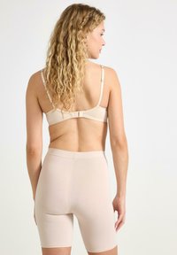 Beige sømløs bralette med justerbare stropper, parret med højtaljede beige shorts, begge med et glat, strækbart stof.