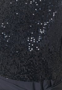 Svart paljetttyg med en glänsande, strukturerad yta; har olika storlekar av paljetter arrangerade i ett skimrande mönster.