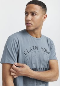 Lyseblå bomull T-skjorte med svart tekstdesign "CLAIM YOUR DENIM", korte ermer, rund hals og en glatt tekstur.