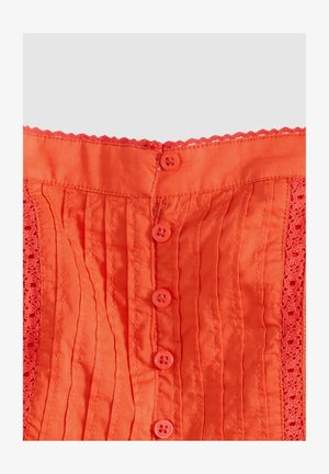 Lys orange stof med lodrette plisseringer, blonder på siderne og en lodret række med seks orange knapper ned foran.