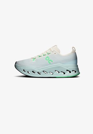 Chaussure de course blanche et bleu clair avec des accents verts, semelle épaisse avec découpes ovales et une boucle au talon, vue de côté.