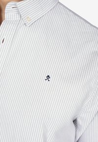 Koszula z guzikami w białe i jasnoniebieskie paski, z małym haftowanym logo w granatowym kolorze na piersi oraz klasycznym krojem kołnierzyka.