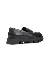 Scarpe slip-on in pelle nera con suola spessa e scanalata e un accento in metallo dorato sulla fascia. Finitura liscia e design minimalista.