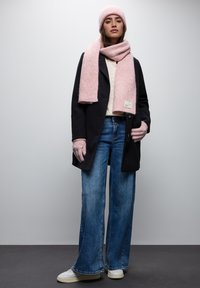 Svart kappa, krämfärgad stickad tröja, rosa scarf och beanie, ljusblå vida byxor och vita sneakers. Mjuka texturer med subtila mönster.