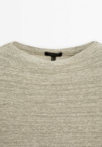 Pull en maille beige clair avec un col rond et une étiquette noire cousue à l'intérieur du col.