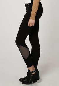 Leggings neri con dettagli in rete al ginocchio, abbinati a stivaletti neri alla caviglia. Il tessuto è elasticizzato e ha una silhouette aderente.