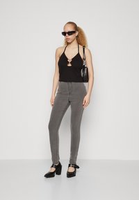 Crna halter majica s detaljem u obliku keyhole, sive uske traperice i crne cipele s potpeticama i remenčićima oko gležnjeva. Model nosi crnu torbu.