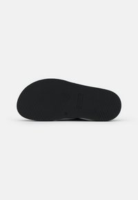 Semelle de chaussure en caoutchouc noir avec une texture nervurée horizontale et verticale, comportant le nom de la marque en relief au centre et un bout arrondi.