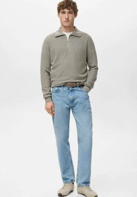 Pullover grigio chiaro con zip, collo rotondo, tessuto morbido. Jeans azzurri, vestibilità dritta. Scarpe beige, design semplice. Sfondo uniforme.