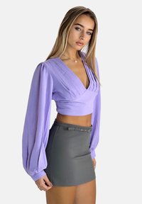 Blusa corta in lavanda con maniche lunghe a sbuffo e design plettato, abbinata a una mini gonna aderente grigia con vita con cintura.