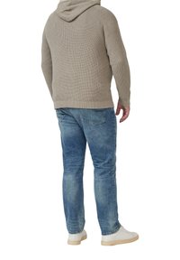 Beżowy dzianinowy hoodie o teksturowanym wzorze, zestawiony z niebieskimi dżinsami i białymi trampkami. Widok pokazuje tył zestawu.