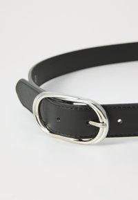 Cinturón de cuero negro con una textura suave, una hebilla ovalada de plata y múltiples agujeros de ajuste a lo largo de su longitud.