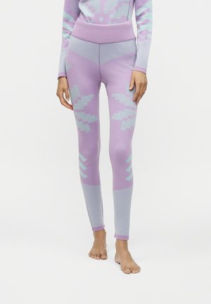 Personne portant des leggings lavande taille haute avec des motifs géométriques bleu clair, debout pieds nus sur un fond blanc.