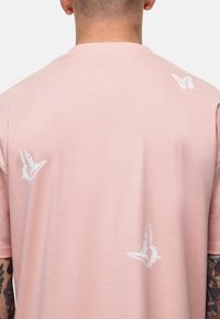 T-shirt rose clair avec des graphismes de papillons blancs au dos. Texture douce avec un col rond classique et des manches courtes.