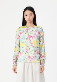 Blouse florale en tissu léger et transparent, mettant en avant un motif de fleurs roses, jaunes et bleues. Manches longues avec des poignets froncés.