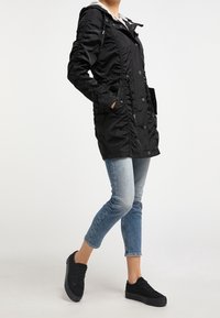 Parka noire imperméable avec coutures latérales à volants, capuche zippée, boutons sur le devant, deux poches latérales et taille ajustable par cordon.