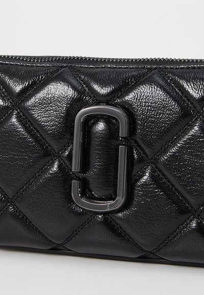 Crni quilted kožni toplić s sjajnom završnom obradom, s istaknutim crnim metalnim detaljem u središtu i zatvaranjem na zip na vrhu.