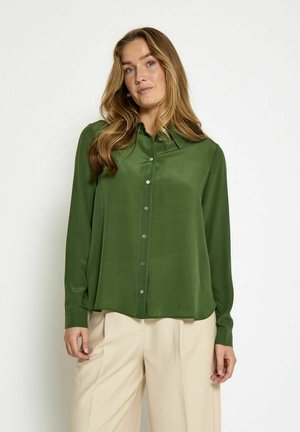 Grüne Bluse mit langen Ärmeln aus glattem Stoff, mit Kragen und durchgehender Knopfleiste, in lässiger Passform. Kombiniert mit beigen Hosen.