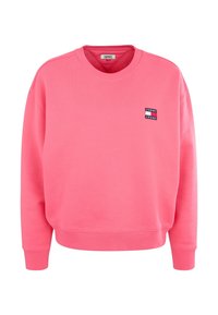 Sweatshirt rose avec col rond, épaules tombantes, poignets et ourlet côtelés. Présente un petit patch logo "Tommy Jeans" sur la poitrine. Texture douce.