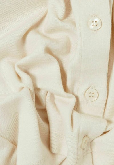 Tissu tricoté couleur crème avec des coutures visibles et trois boutons ressemblant à des perles le long d'une couture verticale.