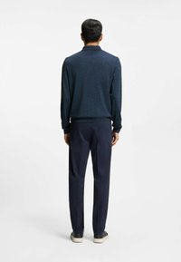 Marinblå stickad tröja med polo-krage, i kombination med mörka byxor. Tyget har en strukturerad yta och har ribbade mudd och nederkant.