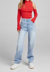 Röd ribbad polotröja med avskuren axeldesign, tillsammans med ljusblå högmidjade jeans och vita sneakers. Slank passform, mjuk textur.