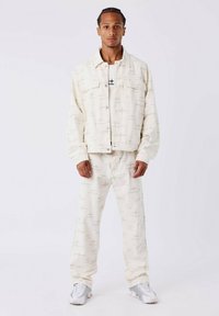 Chaqueta de mezclilla color crema y pantalones a juego con patrones ligeros. La chaqueta cuenta con bolsillos con tapa; el conjunto se complementa con zapatillas blancas.