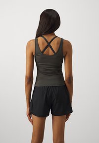 Mørkegrønn tank topp med kryssryggstropper, sammen med svarte shorts. Glatt tekstur, tettsittende design og kontrasterende stroppeDetaljer.