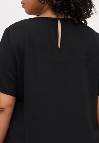 Top nero con scollatura rotonda e apertura a chiave sul retro, maniche corte e tessuto testurizzato. Dettagli di design semplici e funzionali.