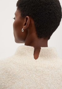 Cremfarbener Strickpullover mit hohem Kragen und einer Schlüsselloch-Detail im Rücken. Glatte Textur und gleichmäßige Nähte. Silberne Creole sichtbar.
