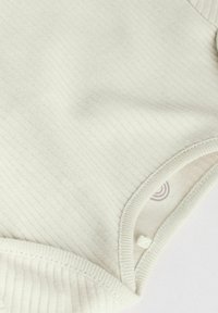 Ljust grått ribbat tyg med en strukturerad mönster, rundade kanter och en svag linjedetalj inuti. Mjukt och flexibelt material.