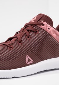 Röd och rosa sportskor med en texturerad ovandel, utrustad med horisontella ränder, en vit sula och en liten logotyp på sidan.