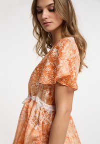 Abito arancione a fantasia realizzato in tessuto leggero, con maniche corte a volant e una cintura in pizzo, decorato con dettagli floreali.