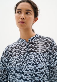 Ilga rankovė blouse, turinti juodą ir šviesiai mėlyną abstraktų raštą, su raukiniais ir apvaliu apykakle. Pagaminta iš lengvos medžiagos.