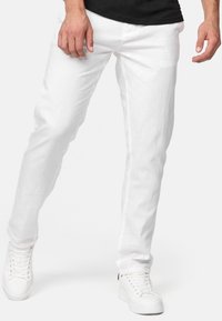 Jeans blancs ajustés en tissu texturé, avec une coupe droite et une esthétique minimaliste. Associés à des baskets blanches.