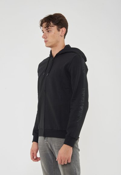 Felpa nera con zip, dotata di cappuccio regolabile, polsini a coste e logo "Emporio Armani" lungo le maniche. Tessuto dalla consistenza liscia.