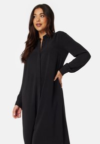 Abito lungo nero a maniche lunghe realizzato in tessuto leggero, con chiusura a bottoni sul davanti, vestibilità comoda e texture liscia con colletto.