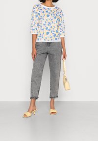 Top leggero a fiori con colori pastello; jeans grigi a vita alta; sandali con tacco gialli; piccola borsa gialla.