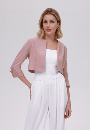 Giacca cropped rosa con una texture liscia, apertura frontale e maniche a metà lunghezza. Abbinata a una maglietta bianca e pantaloni bianchi larghi.