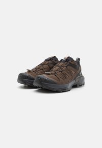 Brązowe buty outdoorowe o solidnej konstrukcji, z oddychającą siateczkową cholewką, bezpiecznym systemem sznurowania oraz grubą, teksturowaną czarną gumową podeszwą.