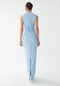 Světle modré šaty bez rukávů s texturovaným povrchem, přiléhavým střihem, rýhováním na zádech a rozparkem na boku.