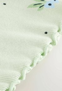 Tissu côtelé vert clair avec imprimé floral, bordure festonnée et surface texturée, présentant de petites fleurs bleues et des points noirs.