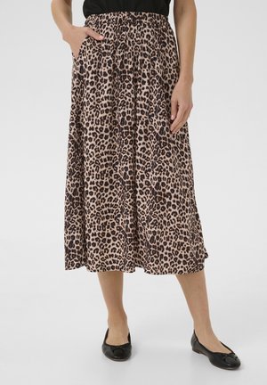Femme portant une jupe midi à imprimé léopard avec des poches, associée à des ballerines noires et un haut noir, debout devant un fond uni.