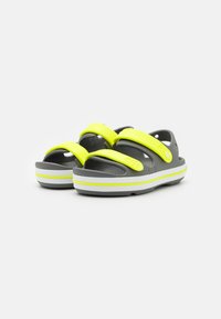 Graue Sandalen mit leuchtend gelben Riemen und weißen Akzenten. Aus Gummi gefertigt, mit einer strukturierten Sohle für besseren Halt und verstellbaren oberen Riemen.