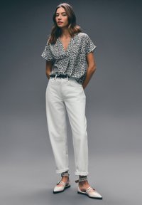 Leopard print short-sleeve blouse, white high-waisted trousers, and pink flats with black accents and ankle straps. Textured fabrics.
