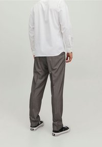 Randiga grå byxor med en lös passform, tillsammans med en vit skjorta med långa ärmar. Svarta sneakers fulländar outfiten.