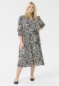Luipaardprint shirt jurk met een ceintuur in de taille, knopen aan de voorkant, lange mouwen en een lengte tot de knie. De stof lijkt glad en lichtgewicht.