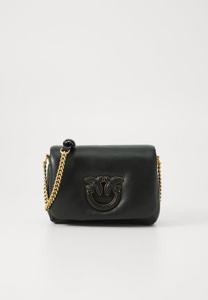 Bolso de mano de cuero negro con una correa de cadena dorada, que presenta un diseño geométrico de cara sonriente con hojas de palma como acentos en la parte frontal.