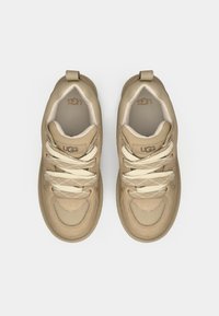 Beige idrettssko med teksturert semsket skinn og mesh, med lyse snøring, rund tå og logodetalj på tungen.